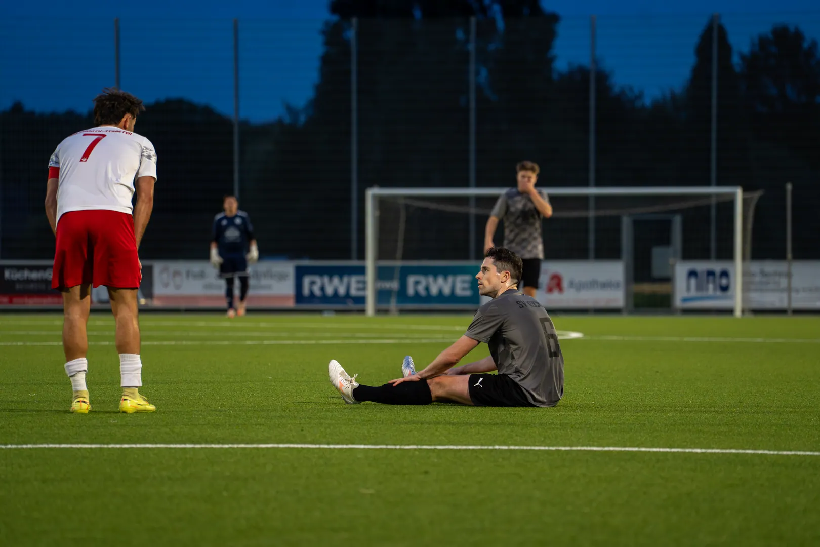 Fußballspieler sitzt erschöpft auf dem Platz unter Flutlicht